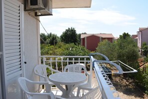 Un balcon avec des chaises et une table en plastique blanc, donnant sur un quartier résidentiel avec des maisons et de la verdure.