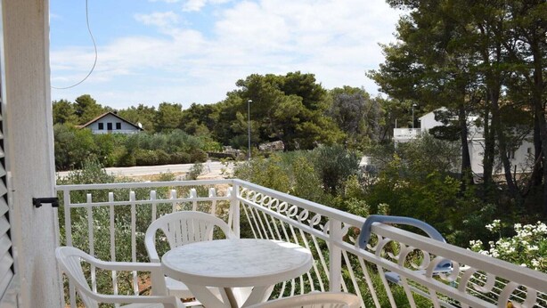 Un balcón con sillas y una mesa blancos, con vista a un jardín con árboles y una casa al fondo.
