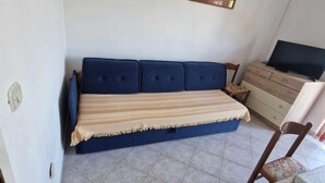 Una habitación con un sofá azul, un televisor sobre un mueble de madera y una silla con una mesita.