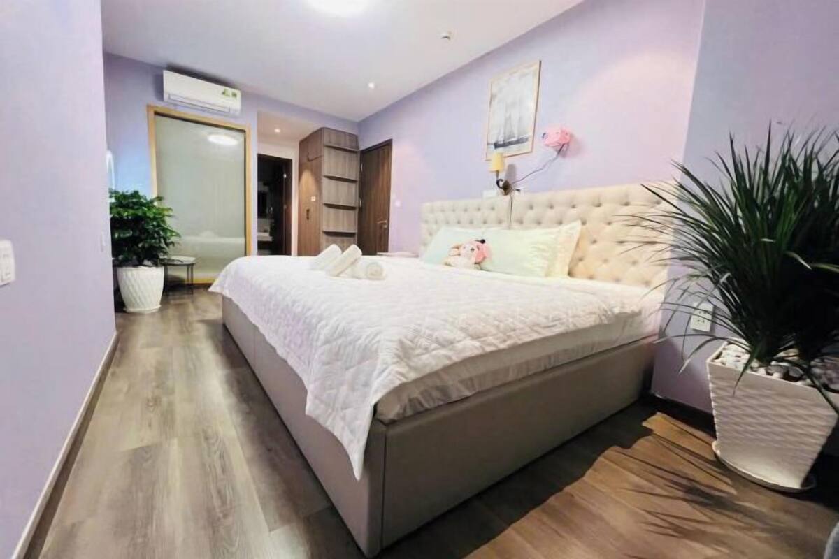 A bedroom with a large bed, a wardrobe, a bedside table, and a potted plant.