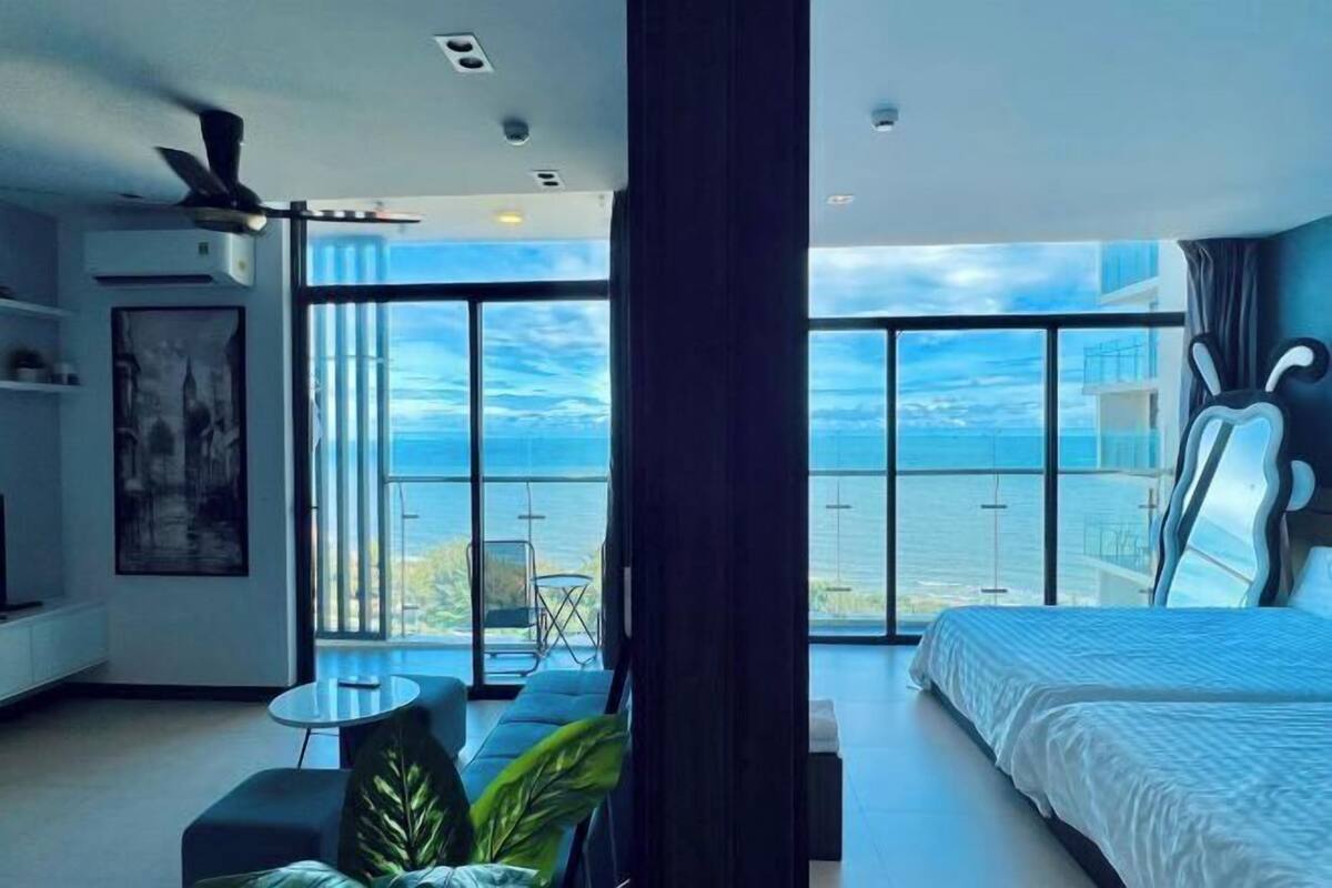 A modern hotel room with a large bed, a seating area, and a balcony with a view of the sea.