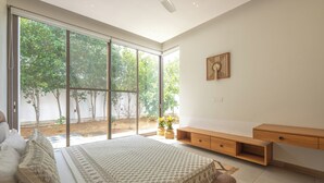 Une chambre avec un grand lit, un banc en bois et une porte-fenêtre coulissante donnant sur un jardin.