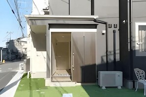 A building entrance with a door, a small step leading up, and a white chair outside. - Lumine Ikebukuro (Tokyo)