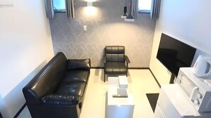 A modern living room with a black leather sofa, a black leather armchair, a white coffee table, a flat-screen TV, and a white coffee maker. - Lumine Ikebukuro (Tokyo)