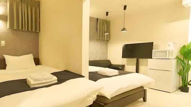 A hotel room with two beds, a flat-screen TV, a microwave, and a potted plant. - Lumine Ikebukuro (Tokyo)