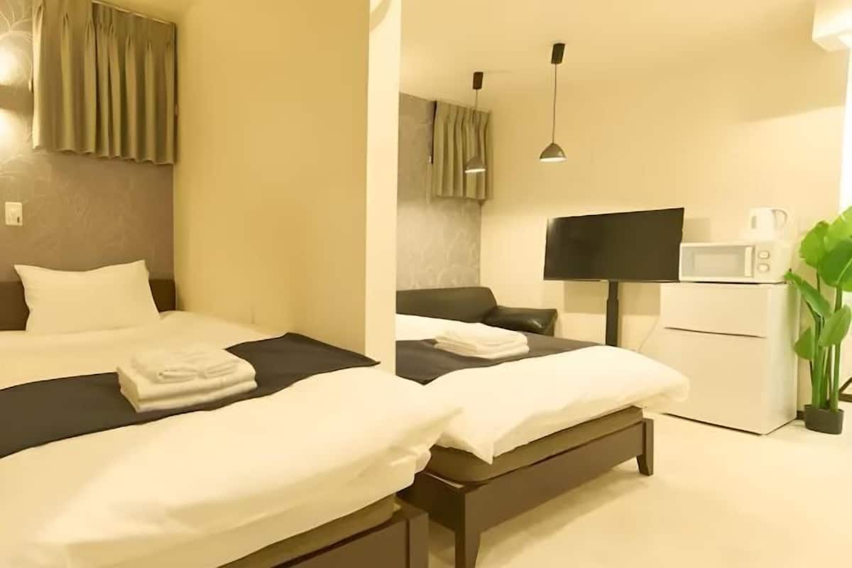Habitación de hotel con dos camas, televisión de pantalla plana, microondas y una planta en maceta.