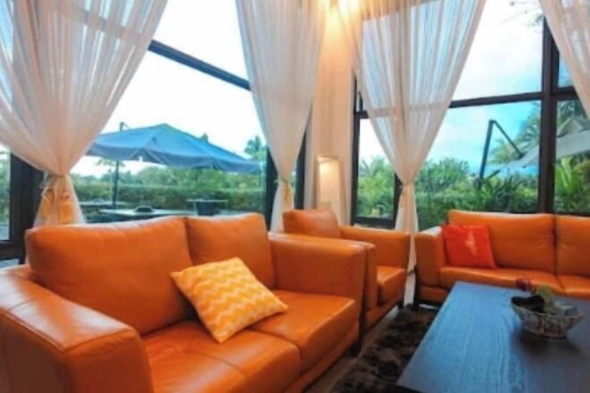 A room with a leather sofa, a coffee table, and sheer curtains.