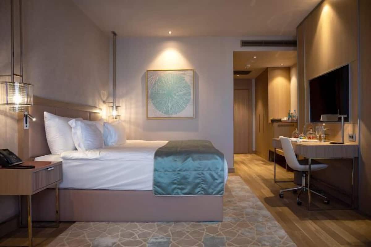 Ein Hotelzimmer mit Bett, Nachttisch, Schreibtisch, Stuhl und einem großen Spiegel.