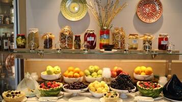 A buffet with various fruits and vegetables, including apples, oranges, and grapes, displayed on a glass counter.