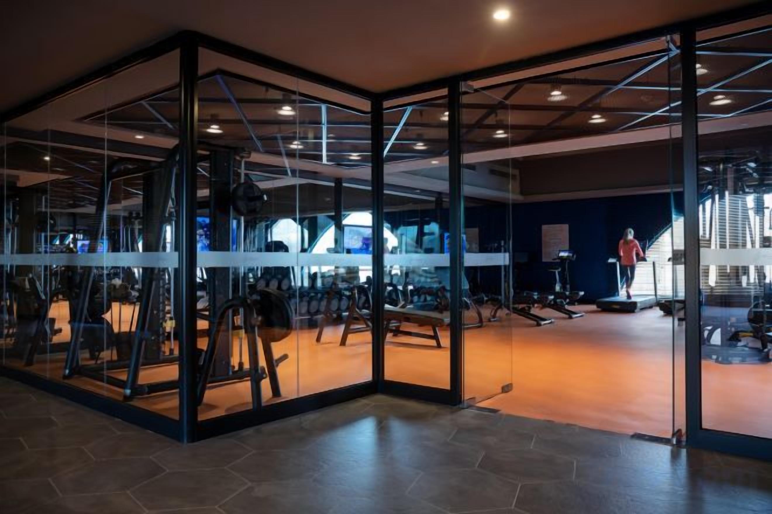 Una sala de gimnàstica amb parets de vidre, equipament esportiu i una escala.