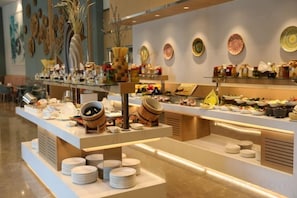 A buffet setup with various dishes and condiments, a counter with plates, and decorative items on the wall. - KARAVANSARAY Turkistan Harbour Hotel - Free FLYING THEATRE Entrance (Turkistan)