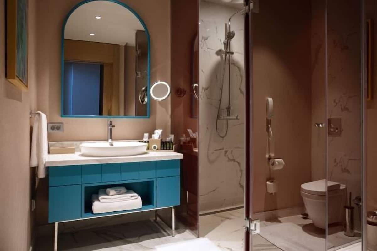 Ein modernes Badezimmer mit einem großen Spiegel, einem Waschbecken, einer Dusche und einer Toilette.