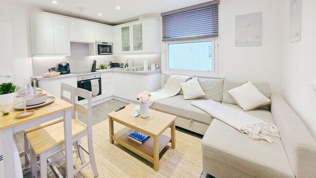 Eine moderne, gut beleuchtete Wohnung mit Küchenzeile, Essbereich und Wohnraum mit Sofa und Couchtisch.
