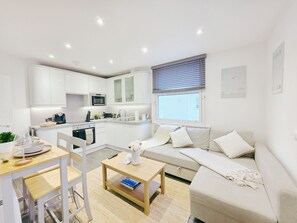 A modern, well-lit apartment with a kitchenette, a dining area, and a living space with a sofa and a coffee table.