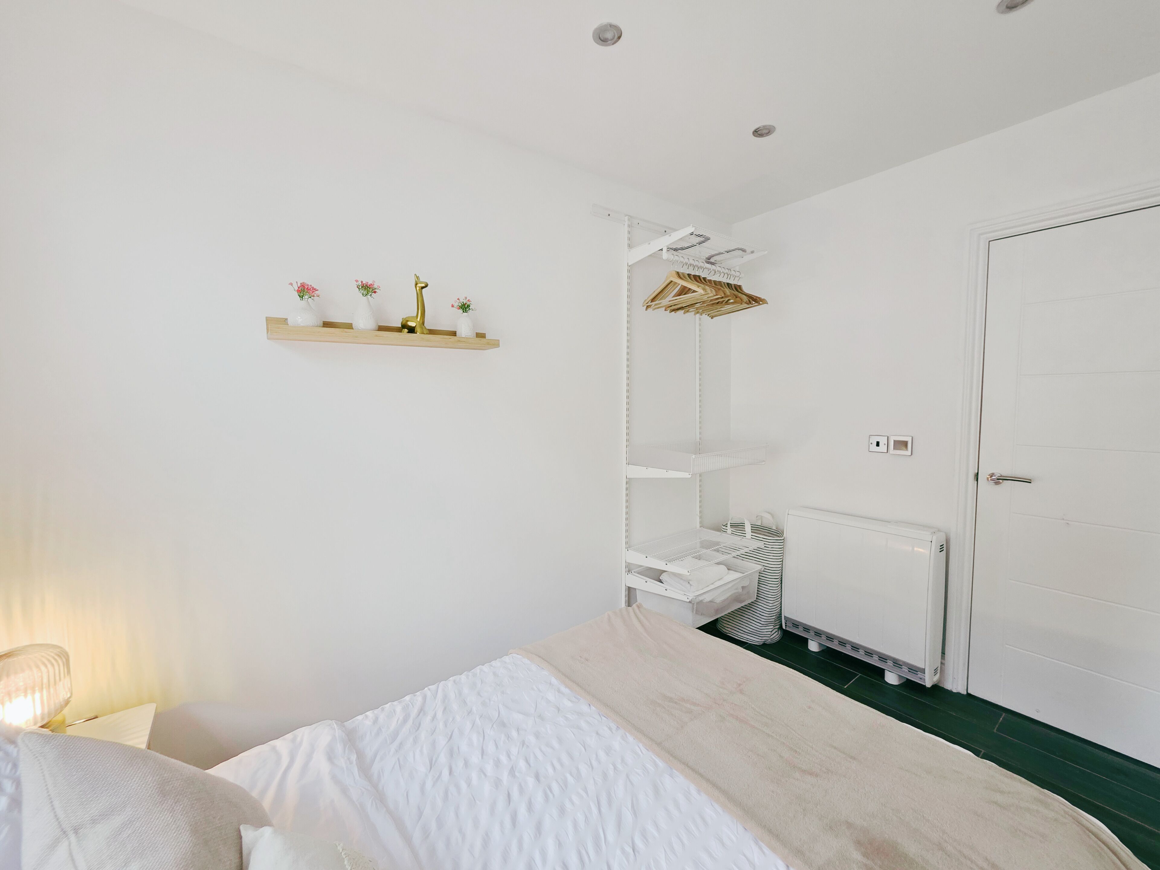 A bedroom with a bed, a radiator, a wardrobe, and a shelf with decorative items.