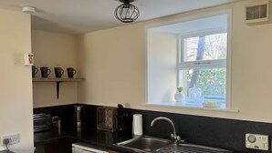 A compact kitchen with a washing machine, a coffee maker, and a window with a view of trees. - Cosy House in the heart of Kirkwall (Kirkwall)