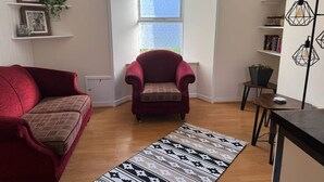 A living room with a red sofa, a patterned rug, a red armchair, and a bookshelf with books and decorative items. - Cosy House in the heart of Kirkwall (Kirkwall)