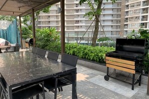 An outdoor patio with a dining table and chairs, a grill, and potted plants. - StayX Condotel (Ho Chi Minh City)
