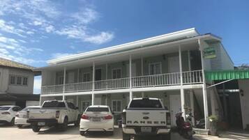 A two-story building with a balcony on the ground floor, parked vehicles in front, and a sign indicating a business.