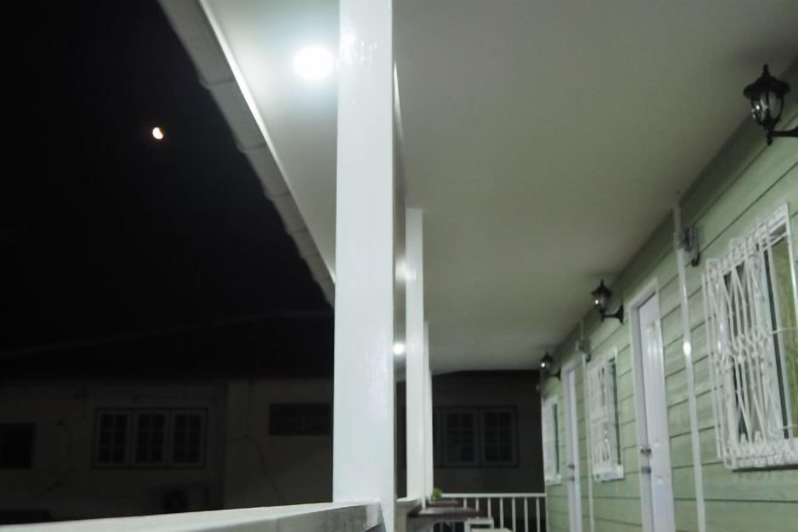 Een balkon met een hekwerk, een wit plafond en een raam met witte luiken.