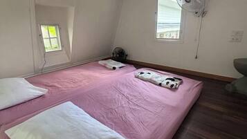 Un dormitorio con una colcha rosa, dos almohadas, un ventilador y una ventana.