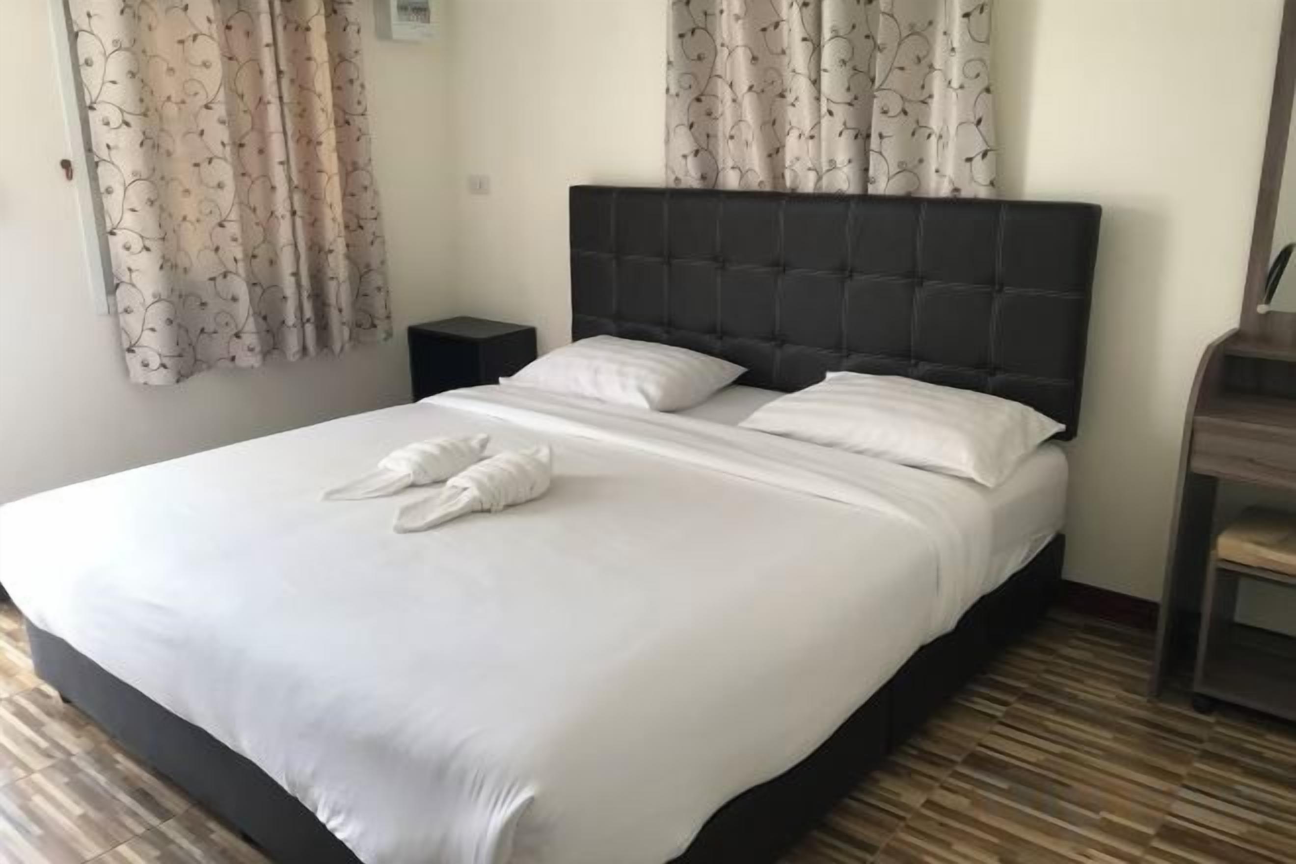 A neatly made bed with white linens and towels, a dark headboard, and a wooden floor.