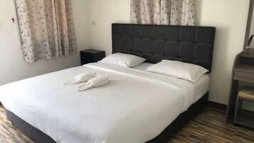 A neatly made bed with white linens and towels, a dark headboard, and a wooden floor.