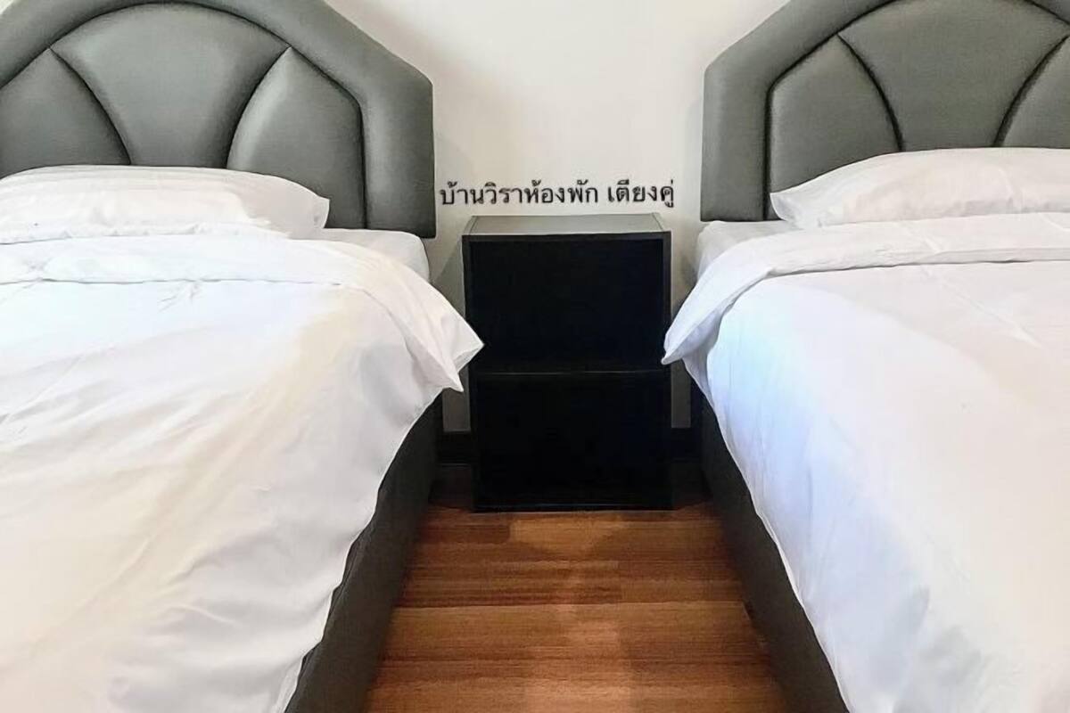 A bedroom with two beds, a nightstand between them, and a wall-mounted shelf.