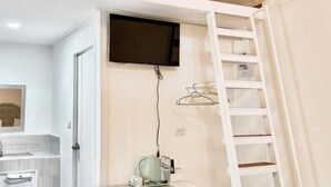 A room with a TV mounted on the wall, a white ladder, and a shelf with hanging items.