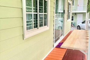 A small porch with a wooden bench, a glass door leading to a balcony, and a white car parked outside. - Baan Wira Guesthouse (Khon Kaen)
