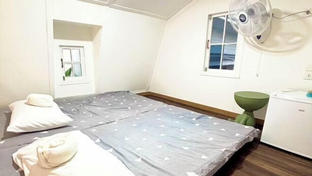 A small, single-bed room with a fan, a small table, and a window.
