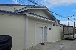 A residential building with a white exterior, a covered entrance, and a parked vehicle. - The Oasis Inn (Hua Hin)