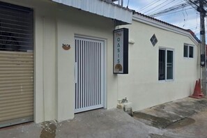 Rakennuksessa on suljettava metallinen rullaovi, valkoinen pystysuoralla raidalla koristeltu portti ja kyltti, jossa lukee: ”The Oasis Hotel”.