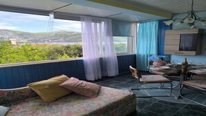 Quarto com cama, mesa de jantar com cadeiras, um lustre e vista para o exterior.