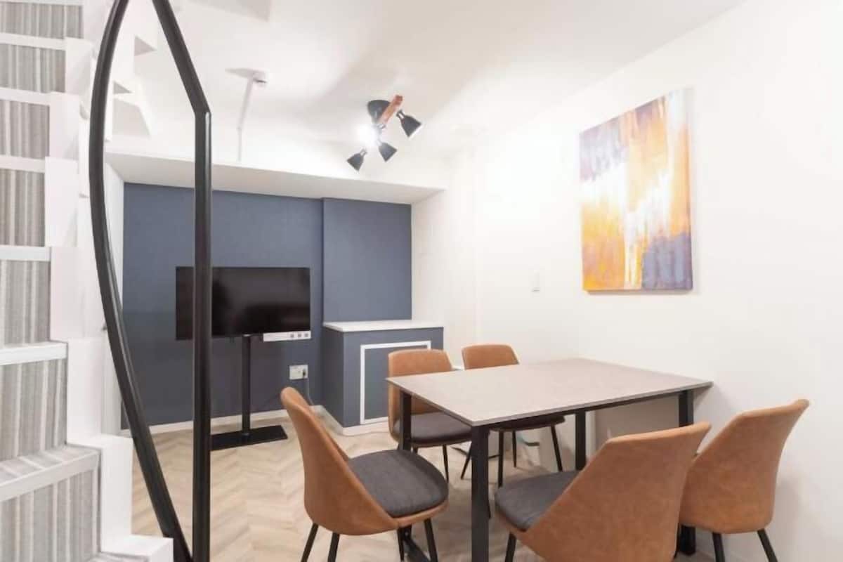 Une pièce moderne comprenant une table à manger, des chaises, un téléviseur et un tableau au mur.