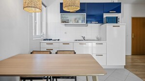 Eine moderne Küche mit weißen Schränken, einer Mikrowelle und einem Kühlschrank. Ein Esstisch mit Stühlen und zwei Hängeleuchten sind ebenfalls vorhanden.