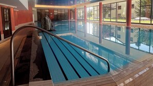 Une piscine intérieure à l’eau d’un bleu cristallin, entourée de murs en verre et surmontée d’un plafond haut.