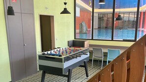 Une pièce avec une table de baby-foot, une fenêtre donnant sur une piscine intérieure et un escalier.