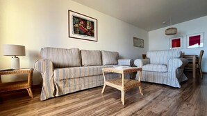 Un salon avec un canapé à rayures, une petite table et une table d’appoint en osier.
