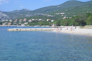 A coastal area with a sandy beach, a pier extending into the water, and buildings in the background.