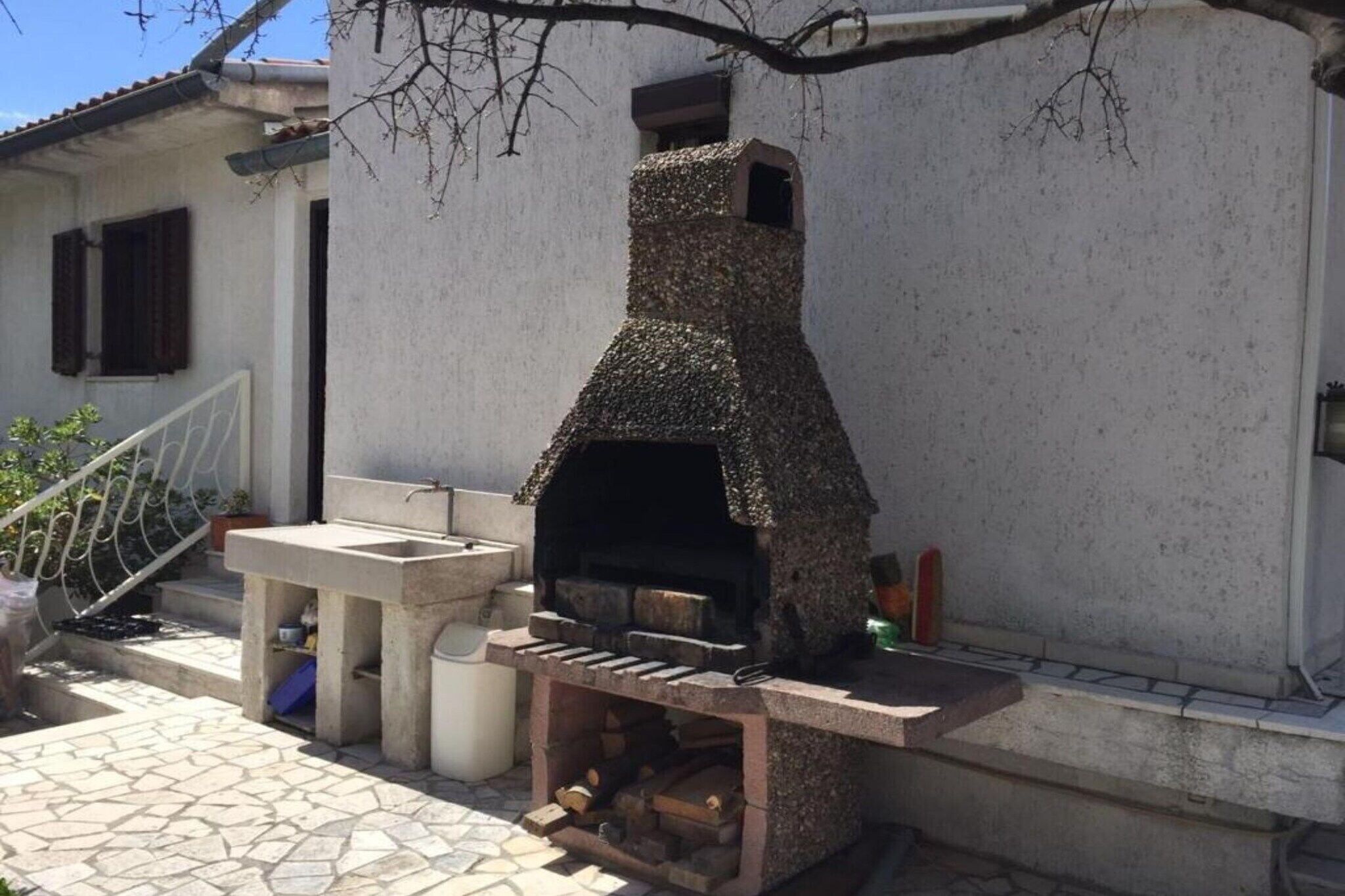 Un horno de piedra para pizzas al aire libre con una chimenea, una mesa pequeña con un lavamanos y un espacio para almacenar leña.