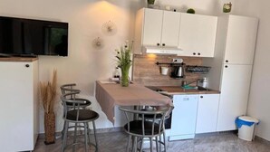 Eine moderne Küche mit weißen Schränken, einem eingebauten Ofen und einer Spüle. Es gibt drei Barhocker und einen kleinen Tisch mit einem Blumenstrauß.