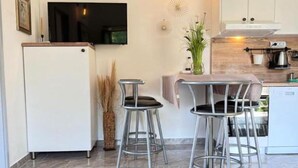 Eine moderne Küche mit einem weißen Kühlschrank, zwei Metall-Barhocker, einer Holz Arbeitsplatte und einem kleinen Esstisch.