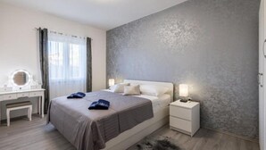 Ein Schlafzimmer mit einem Bett, Nachttischen, einem Schminktisch mit Spiegel und einem Fenster mit Vorhängen.