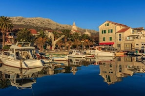 A harbor with boats docked, a church with a bell tower, and buildings with red awnings.