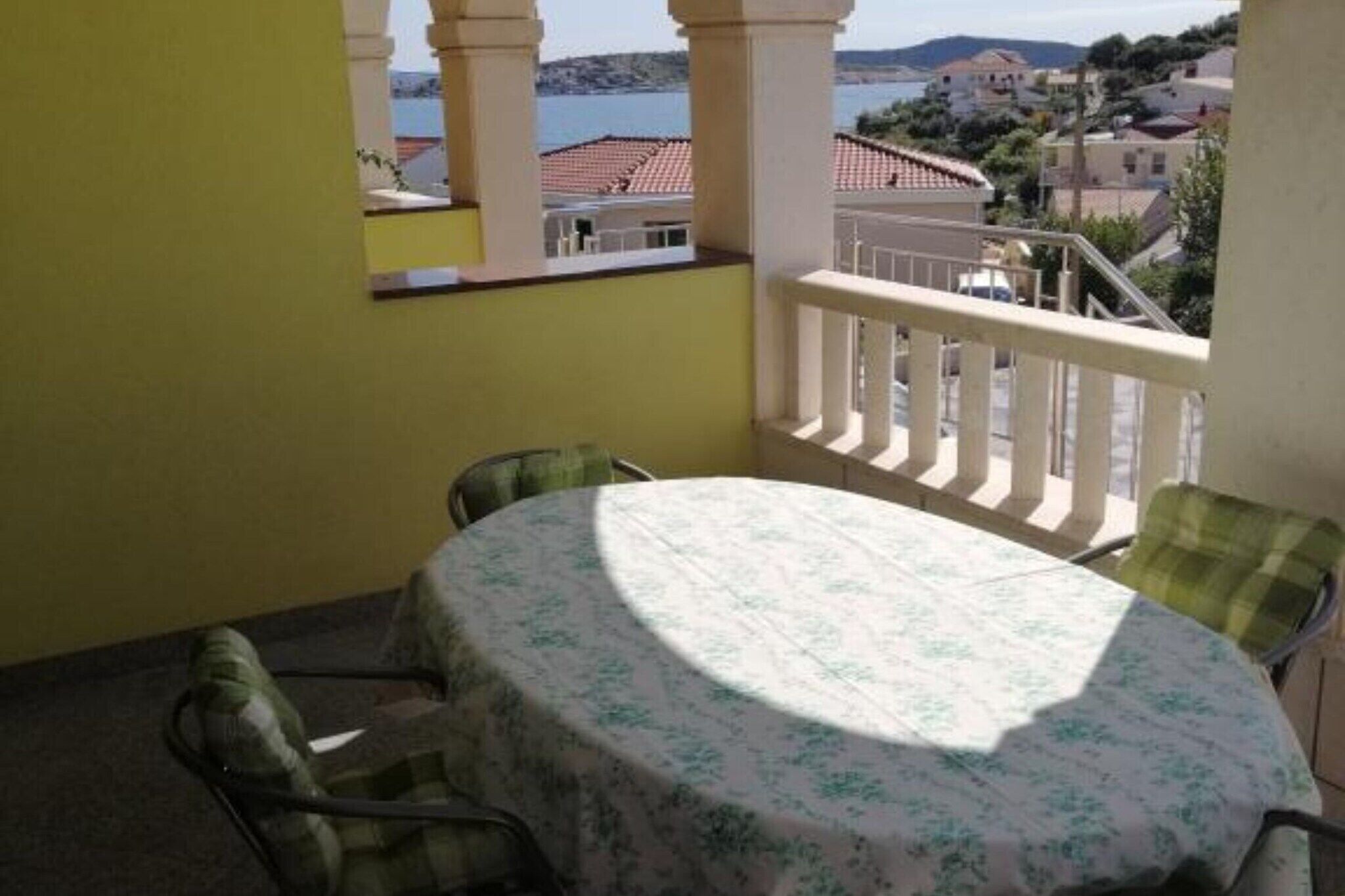 A balcony with a round table and chairs, overlooking a coastal area with buildings and a body of water.
