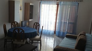 Una habitación con una mesa de comedor redonda, sillas, un sofá, un televisor y una ventana con cortinas.