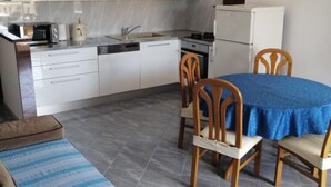 Cocina compacta con armarios blancos, un fregadero y una estufa. Hay una mesa de comedor con mantel azul y cuatro sillas de madera.