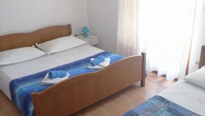 Una cama individual con cabecera de madera, una mesita de noche con lámpara y una ventana con cortinas.
