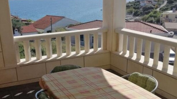 A balcony with a table and chairs, overlooking a coastal area with houses and the sea.